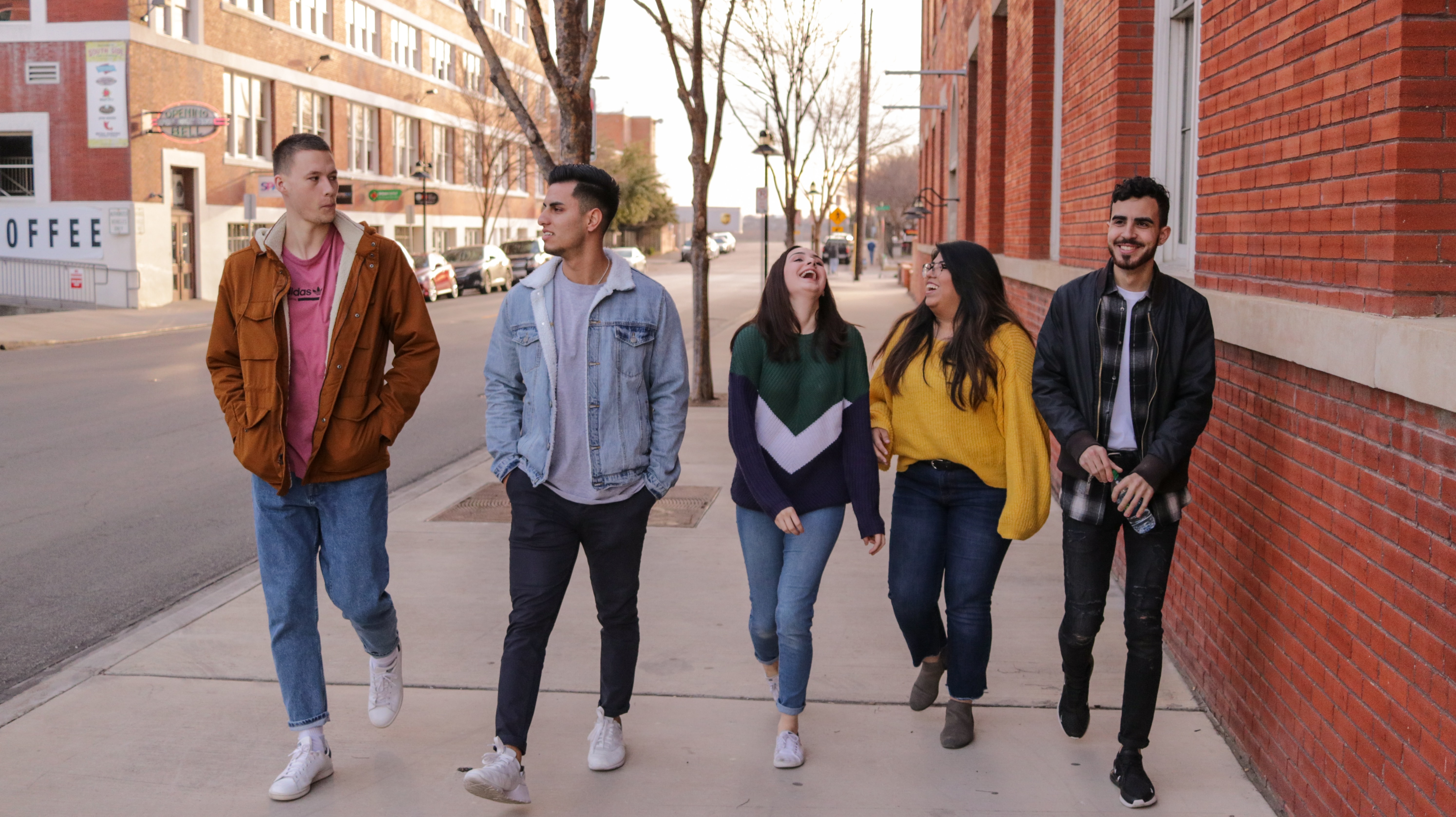 Five youth happily walking down a city street and laughing together.